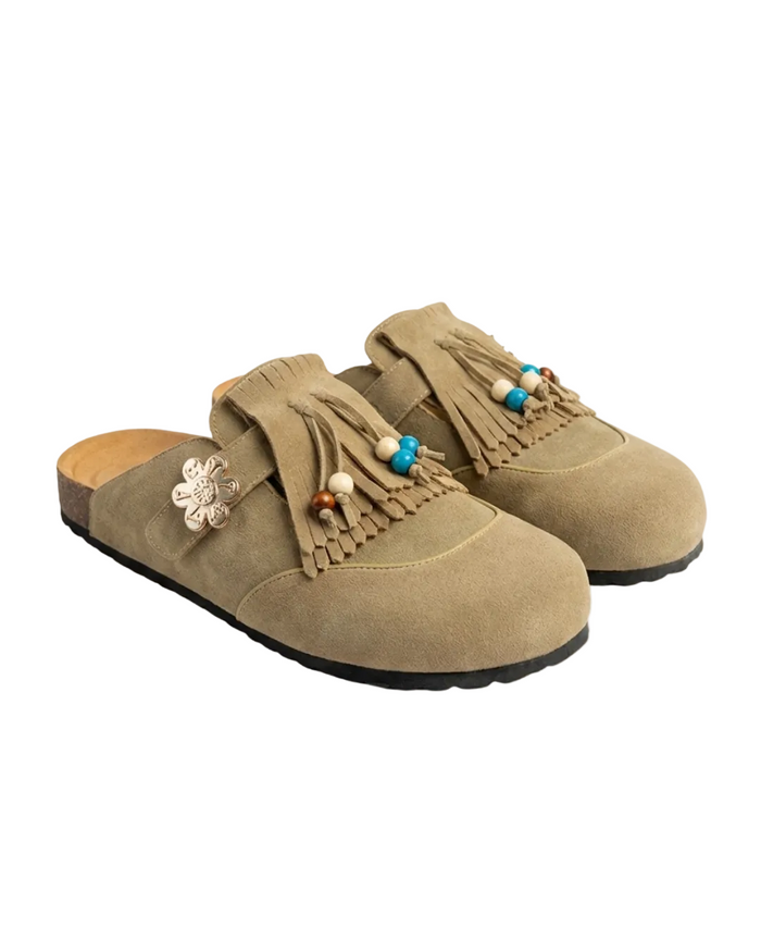 Pair of latte suede slippers with tassels and decorative elements on a white background