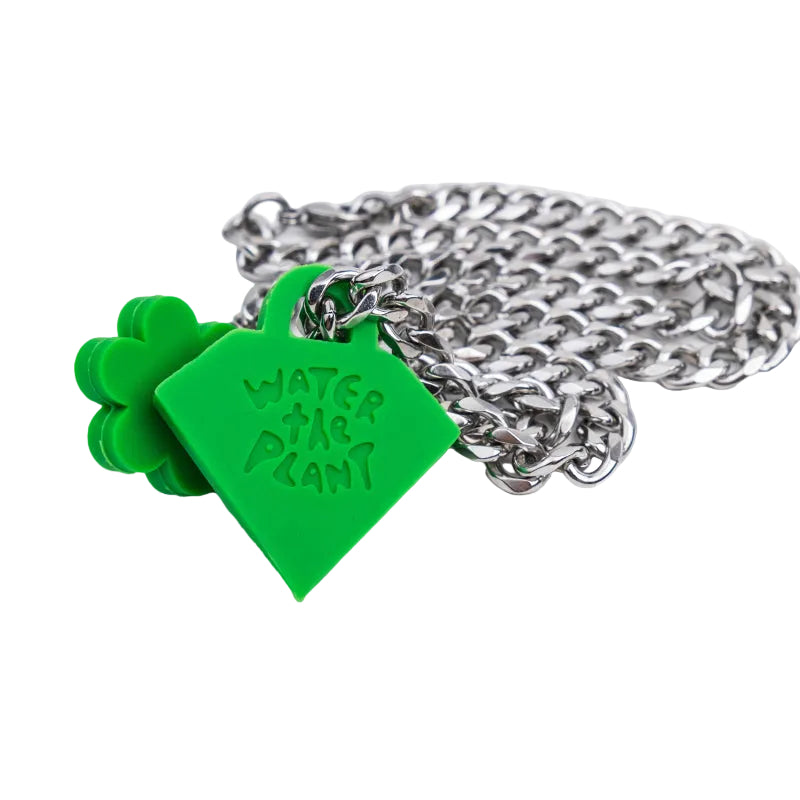 A silver metal chain necklace with a bright green heart-shaped tag engraved with 'WATER THE PLANT' and a matching green four-leaf clover charm, shown on a plain white background.
