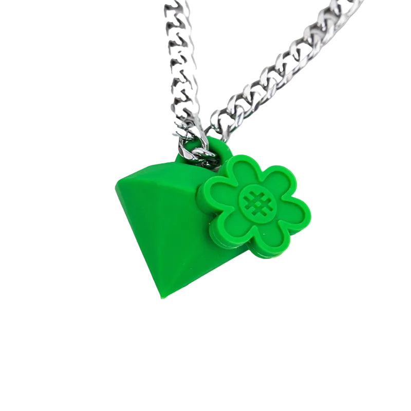 A close-up of a silver chain necklace with a bright green pendant shaped like a diamond, adorned with a small green flower charm featuring a hashtag symbol in the center, set against a plain white background.
