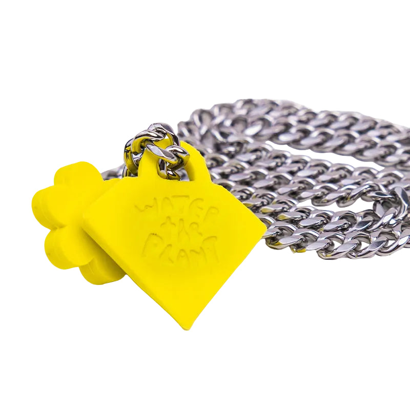 A close-up of a silver chain necklace with a bright yellow house-shaped pendant featuring the text 'WATER THE PLANT' in a stylized font, set against a plain white background.