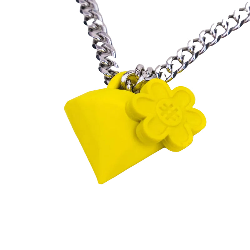 A close-up of a silver chain necklace featuring a bright yellow diamond pendant with a small yellow flower charm attached, set against a plain white background.