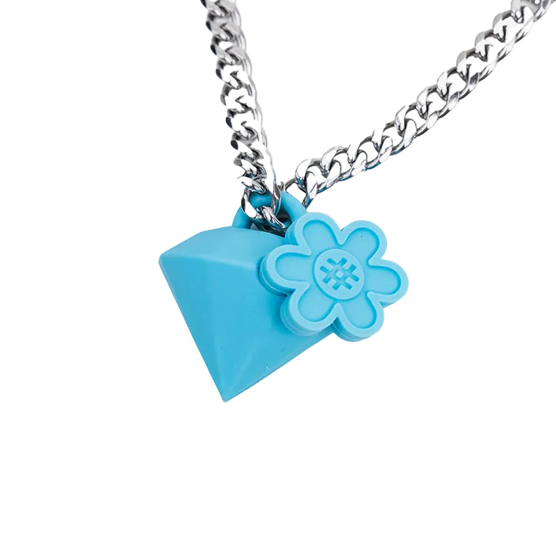 A silver chain necklace featuring a bright blue pendant shaped like a faceted diamond, adorned with a small 3D flower charm on the side, set against a plain white background.