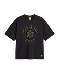 A black short-sleeve t-shirt with a green camouflage graphic on the front that reads 'WATER THE PLANT' around a flower motif, shown on a plain white background.